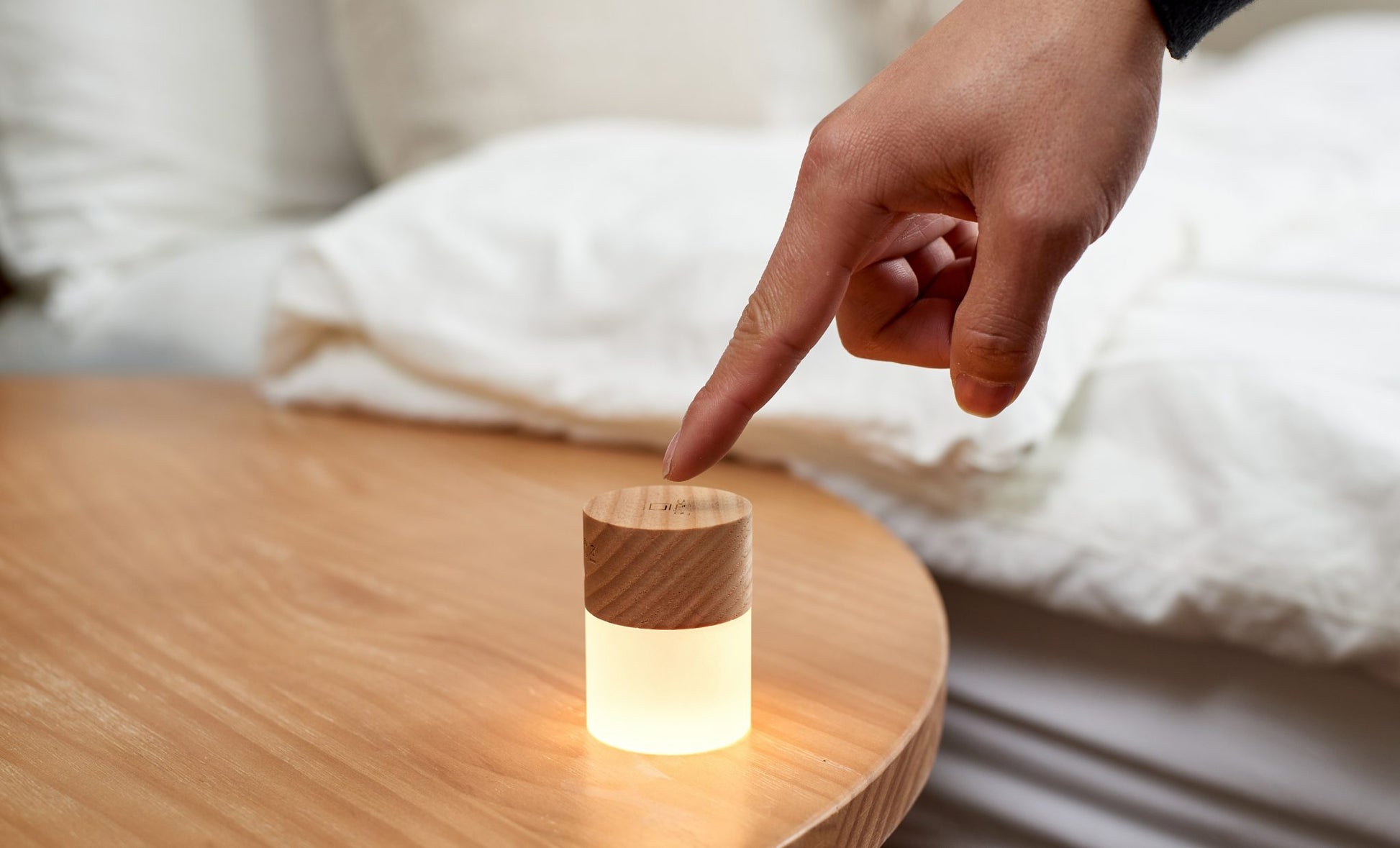 Minimalistyczna lampka nocna z drewna jesionowego dotykana na drewnianym stoliku obok łóżka