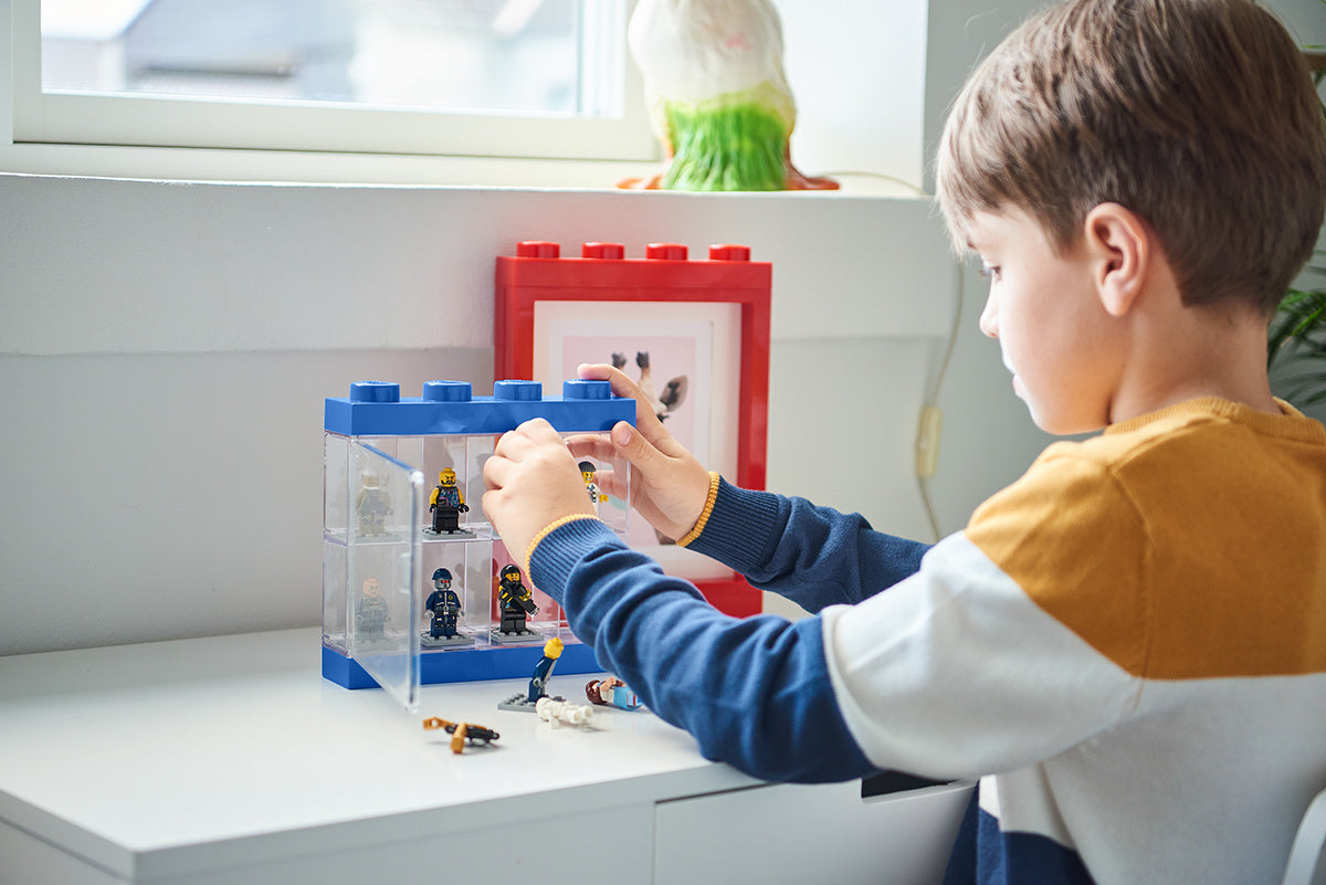 Chłopiec bawiący się gablotką na minifigurki LEGO w kształcie klocków, ustawioną na białym biurku