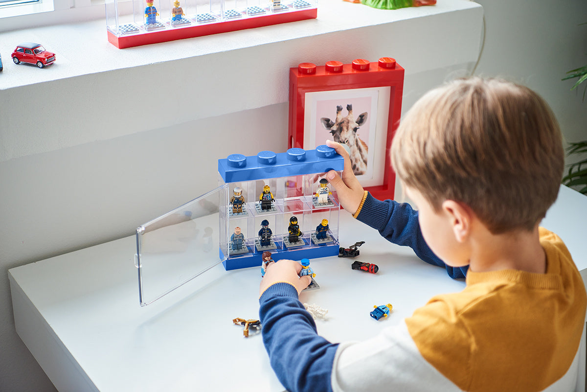 Chłopiec bawi się gablotką na minifigurki LEGO firmy BV JACOB COMPANY z przezroczystymi półkami i kolorową ramką