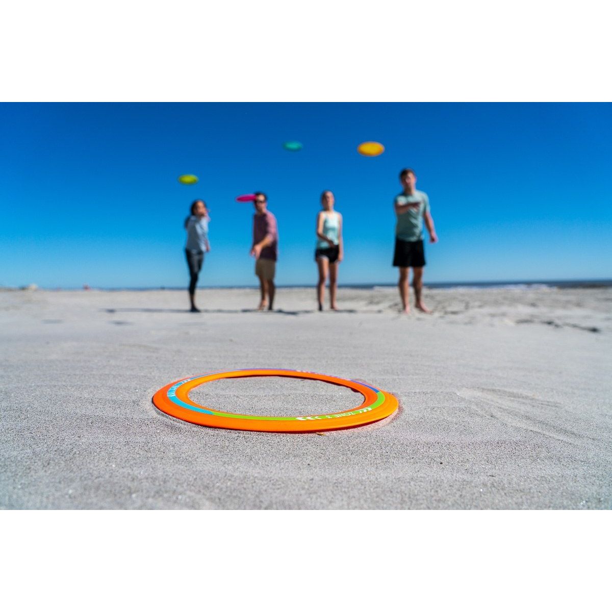 Cztery osoby grające na plaży w gra Waboba Backnine z kolorowymi frisbee i celującymi pierścieniami