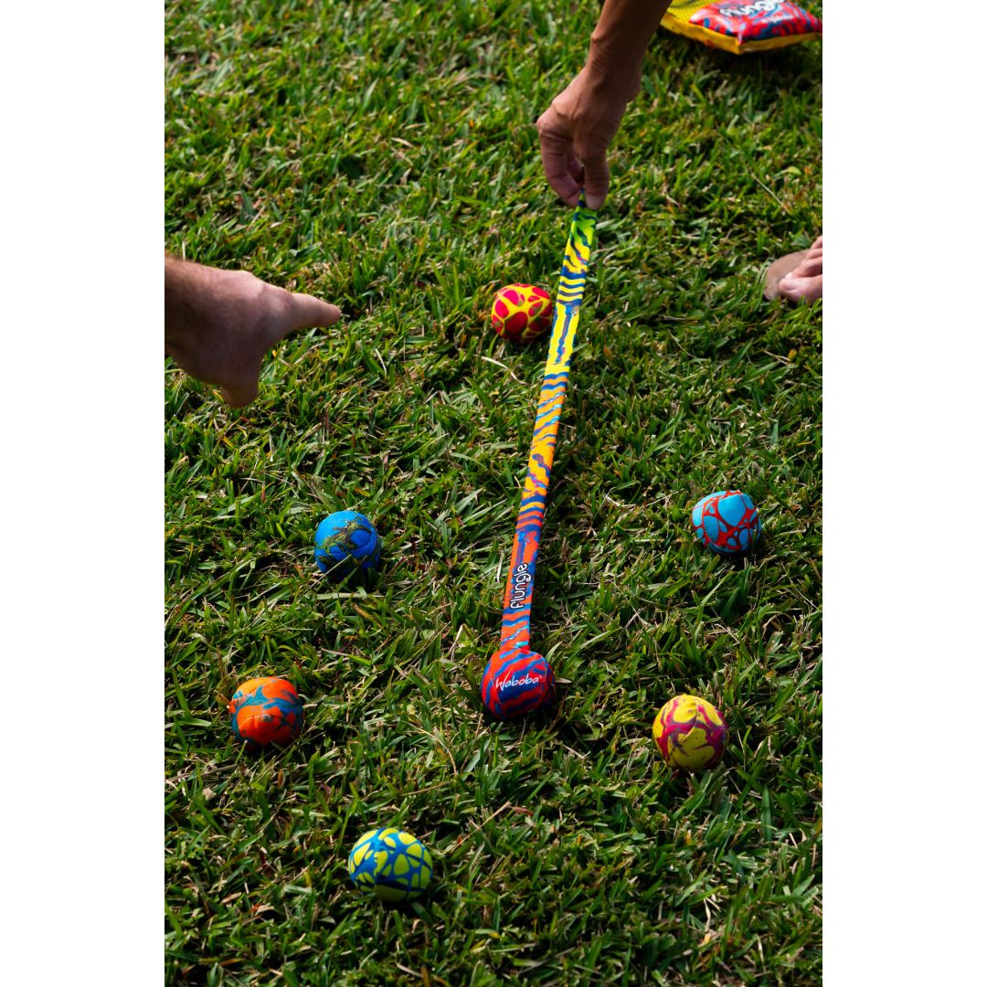 Gra zręcznościowa Waboba Flungle na trawie z kolorowymi piłkami i kijem do uderzania