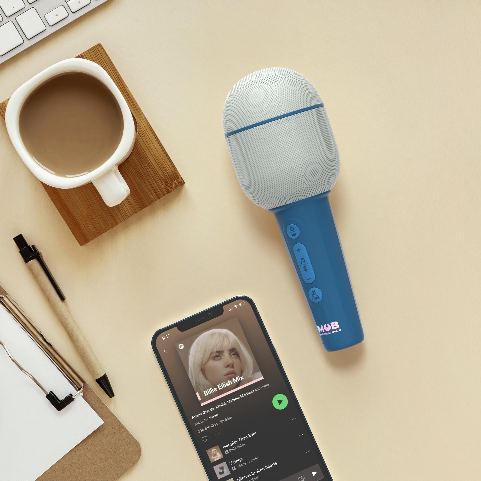 Mikrofon bezprzewodowy z efektami w kolorze niebieskim obok smartfona z odtwarzaną muzyką i kubka kawy
