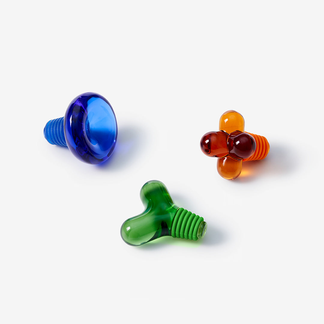 Niebieski korek do butelek Areaware obok zielonego i pomarańczowego korka do butelek