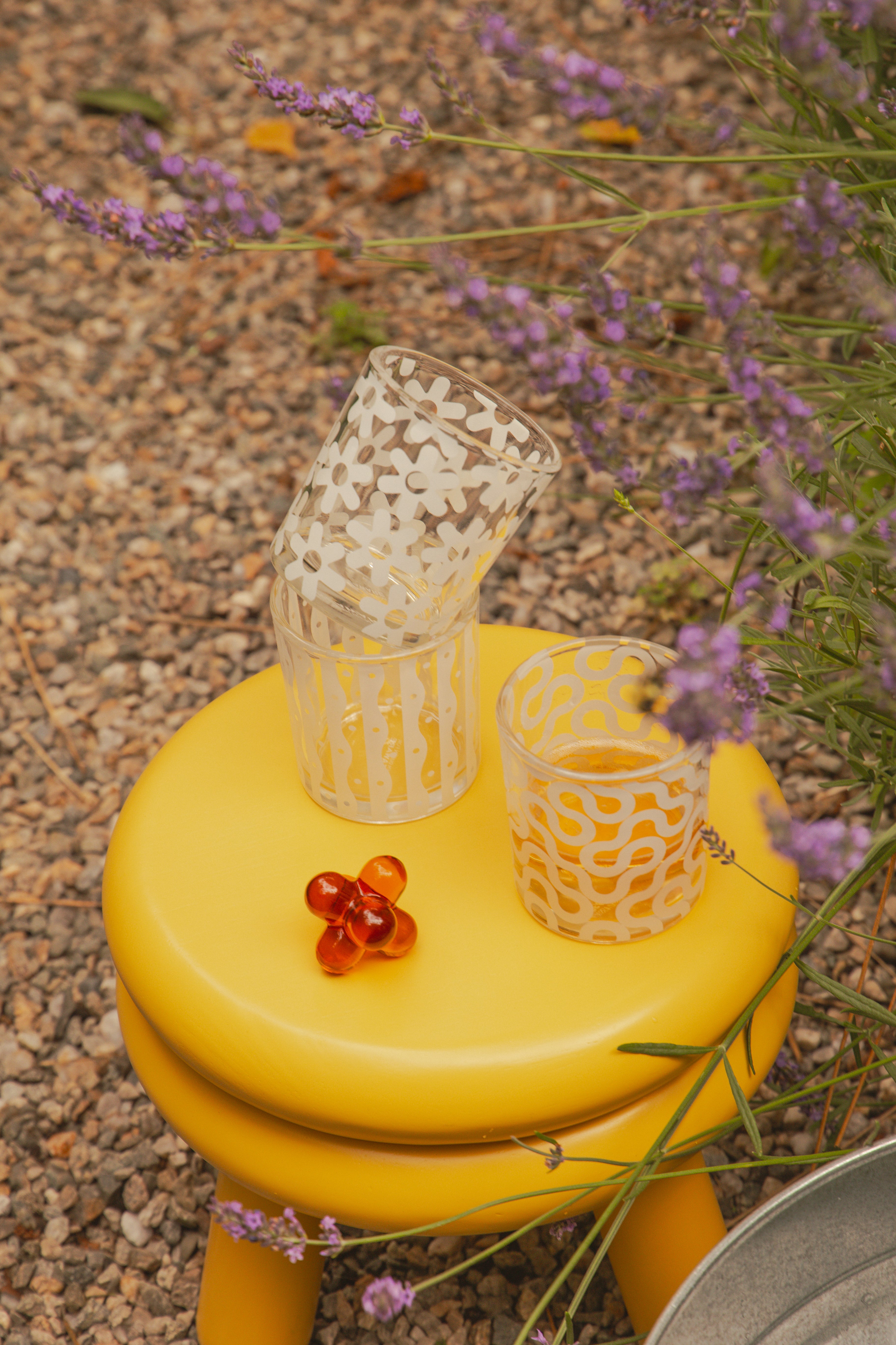 Korek do butelek designerski w pomarańczowym kolorze na żółtym stołku obok szklanek z wzorami