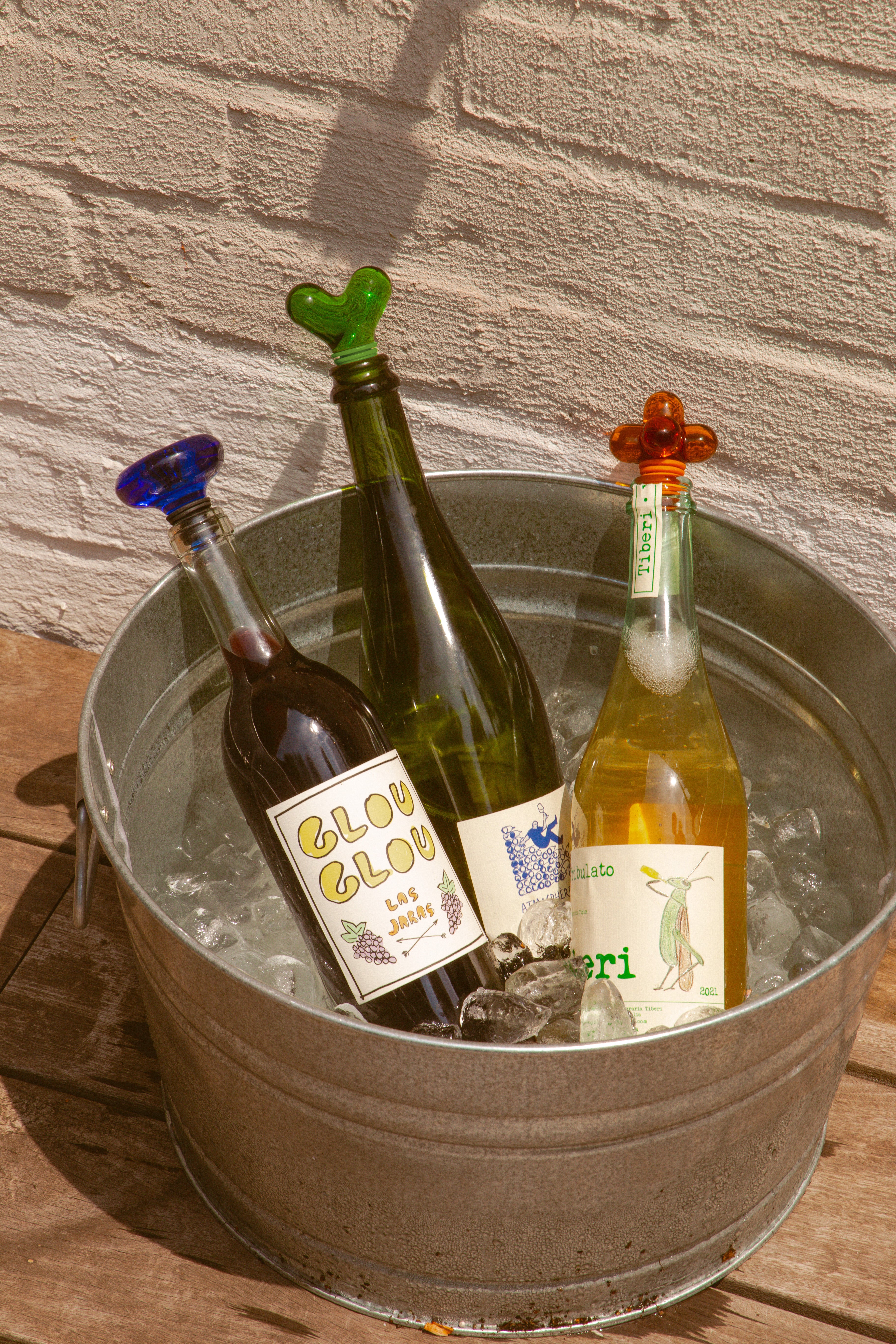 Korek do butelek niebieski od Areaware na butelce z winem w metalowym wiadrze z lodem