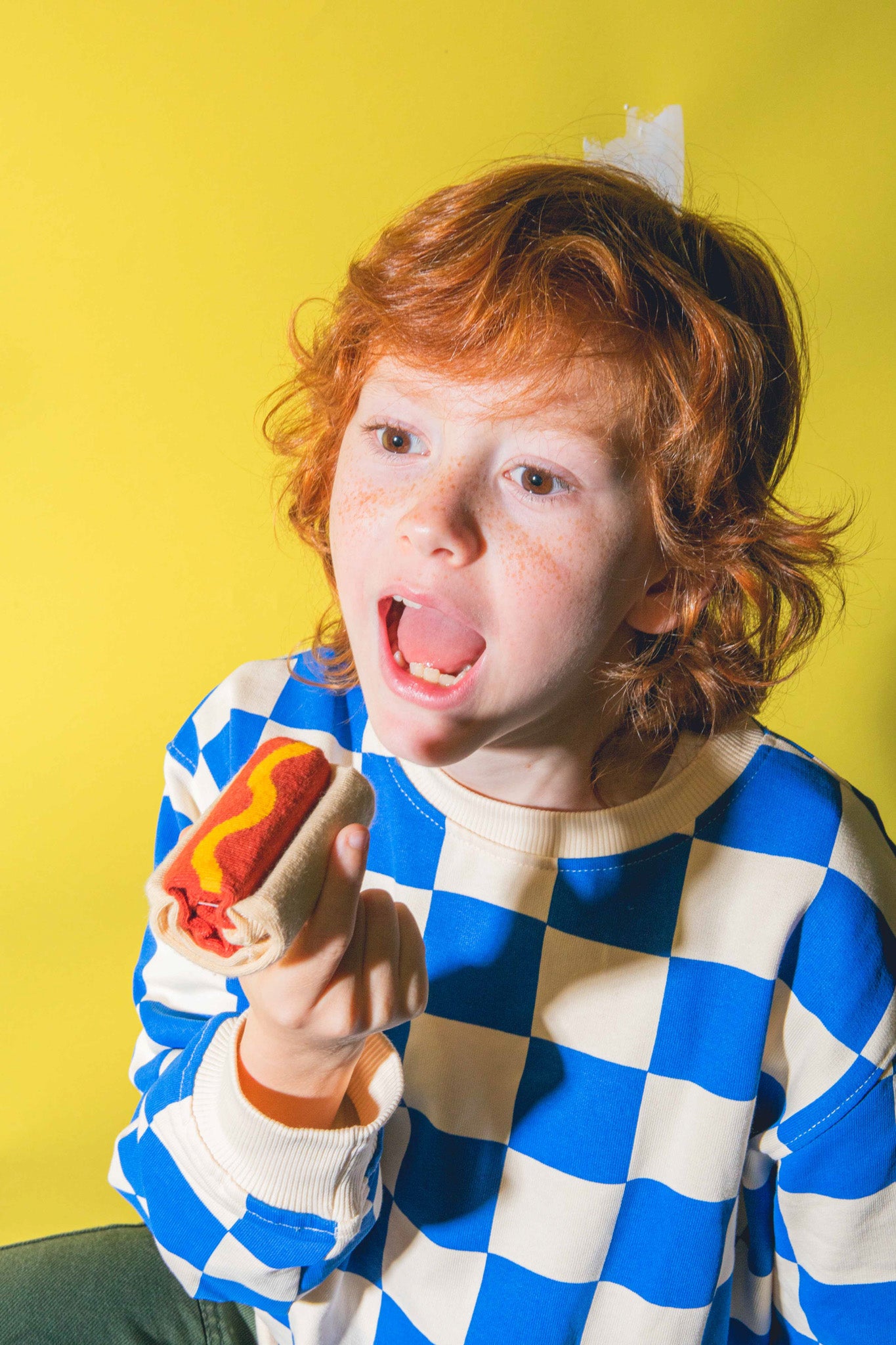 Dziecko trzymające skarpetki hot dog dla dzieci na żółtym tle w niebiesko-białej bluzie