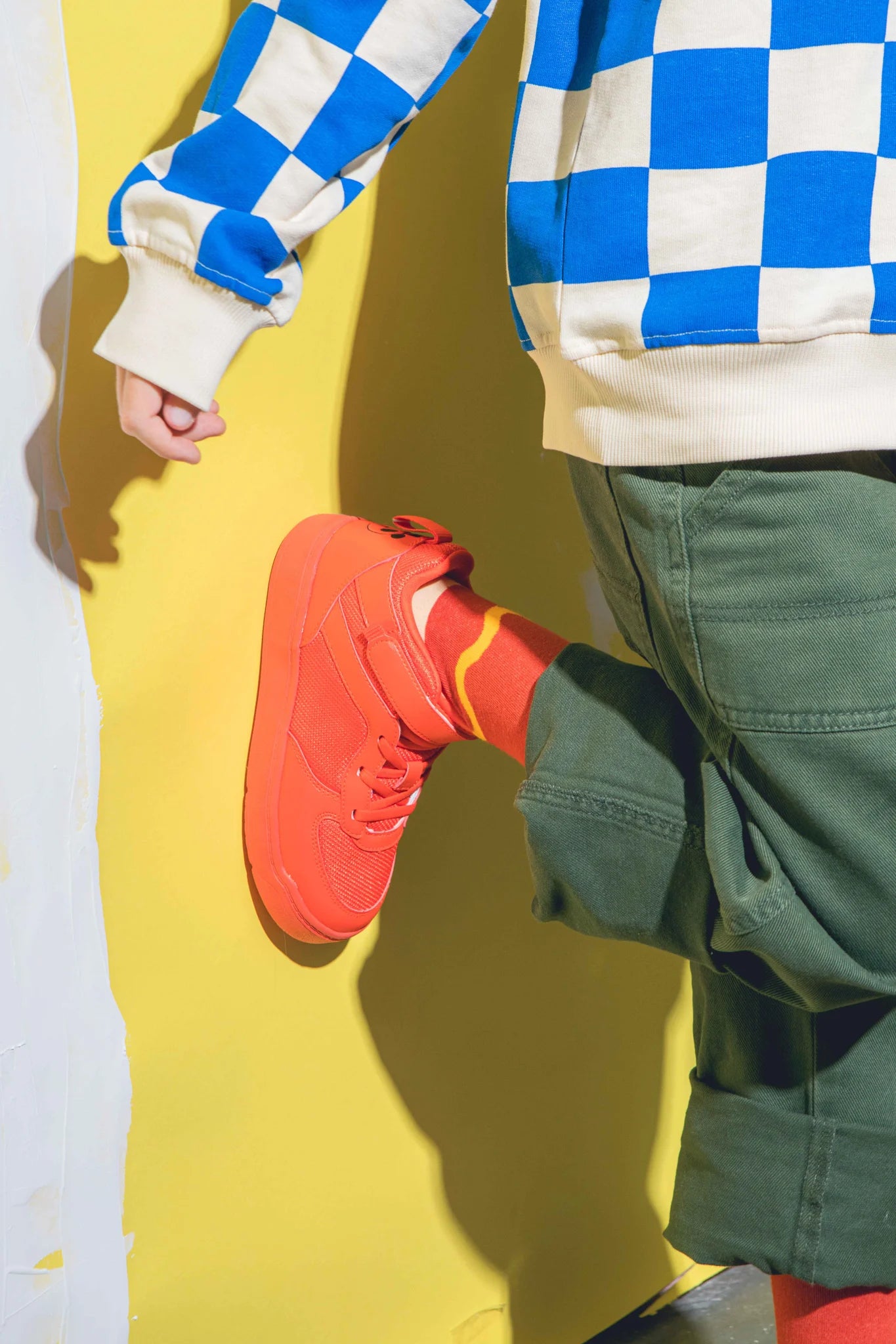 Skarpetki hot dog dla dzieci w pomarańczowym kolorze na nodze dziecka ubranej w zielone spodnie i niebiesko-białą bluzę