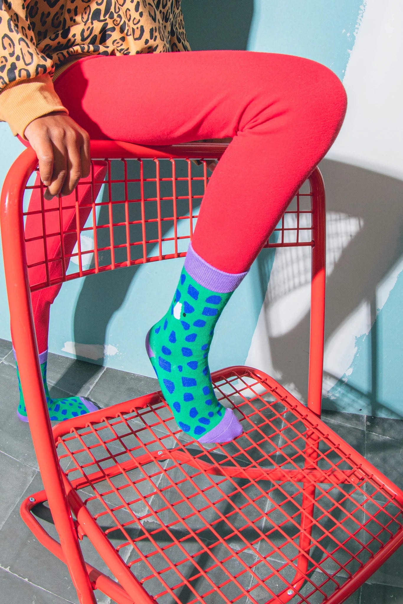 Skarpetki dinozaur dla dzieci w zielono-niebieskie łaty na stopach dziecka siedzącego na czerwonym krześle