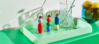 Otwieracz do butelek Abaco Areaware w kolorowych kształtach na zielonym tle z szklanką i cytrynami