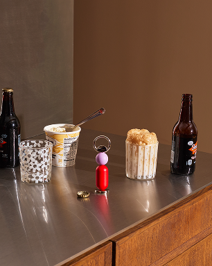 Otwieracz do butelek Abaco Areaware czerwony na metalowej powierzchni obok napojów i przekąsek