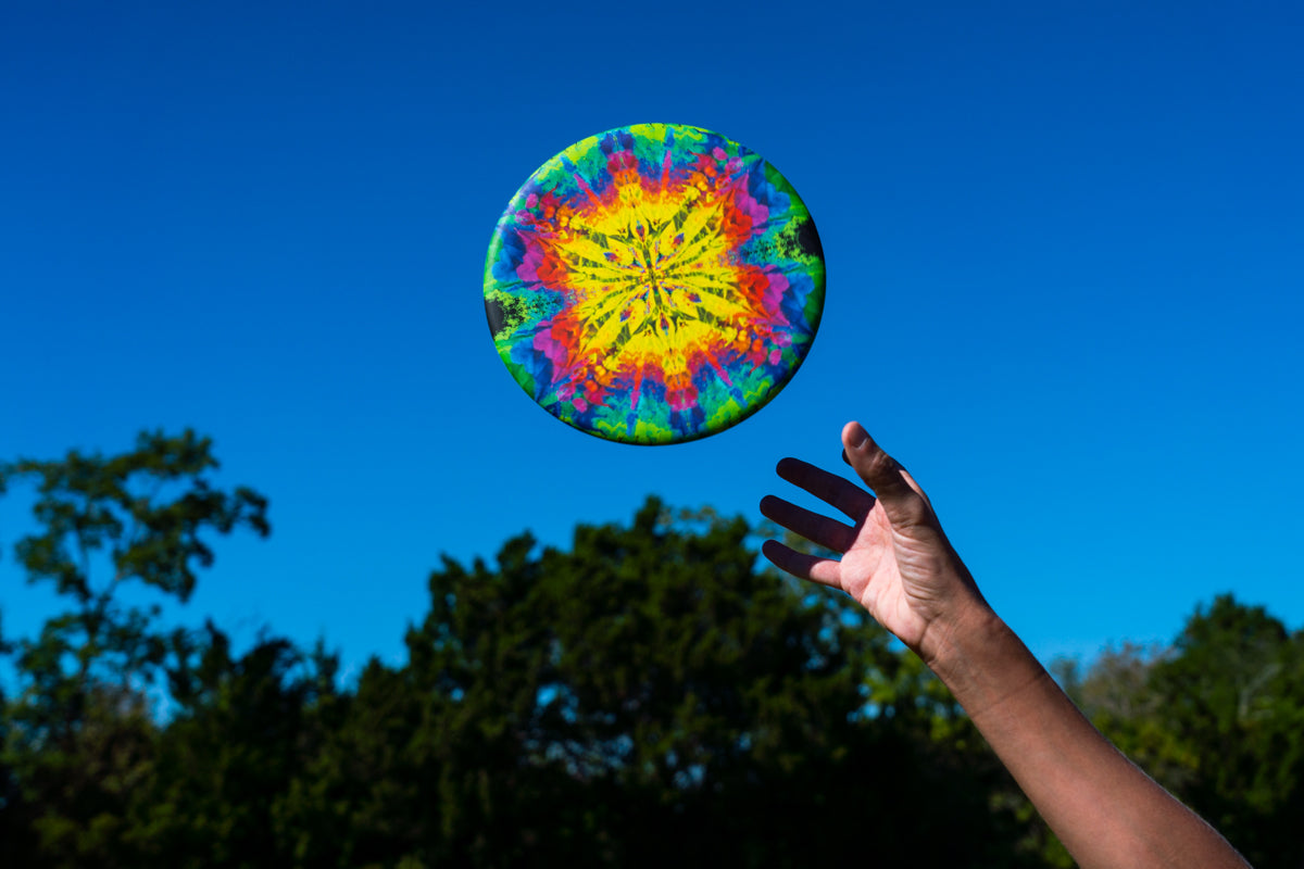 Kolorowy frisbee Waboba Wingman Pro unoszący się w powietrzu na tle niebieskiego nieba i zielonych drzew