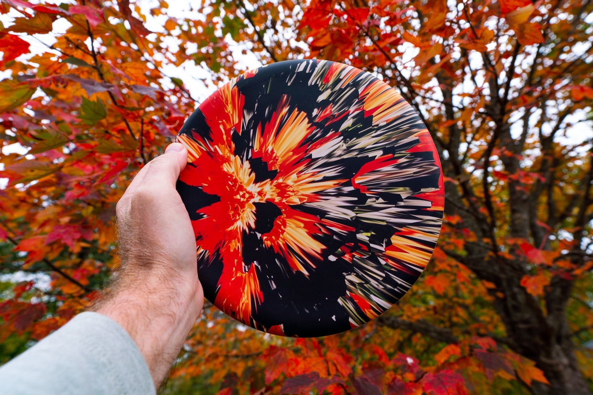 frisbee Waboba Wingman Pro w czerwono-czarne wzory trzymane na tle jesiennych liści