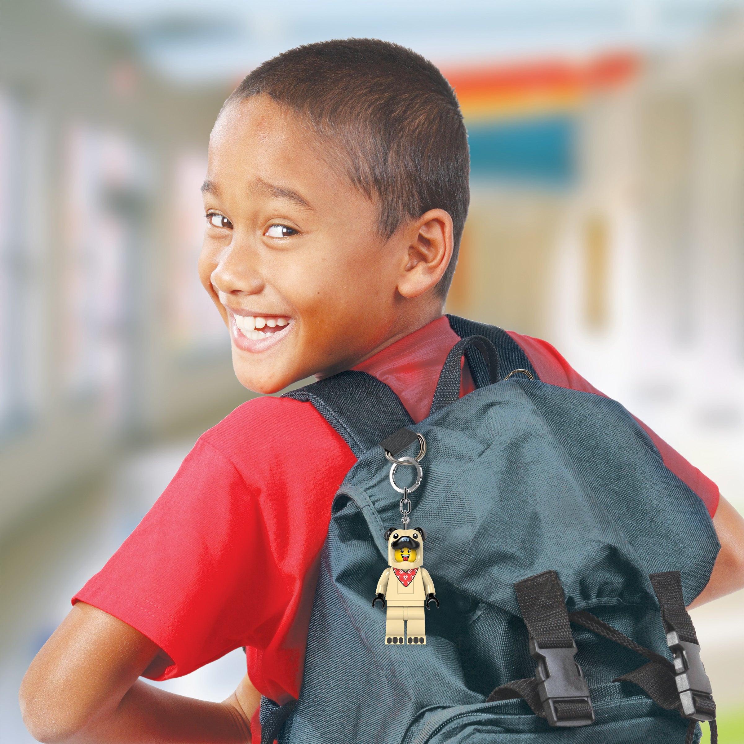 Dziecko z uśmiechem i plecakiem z brelokiem z latarką LEGO Mops od MOB