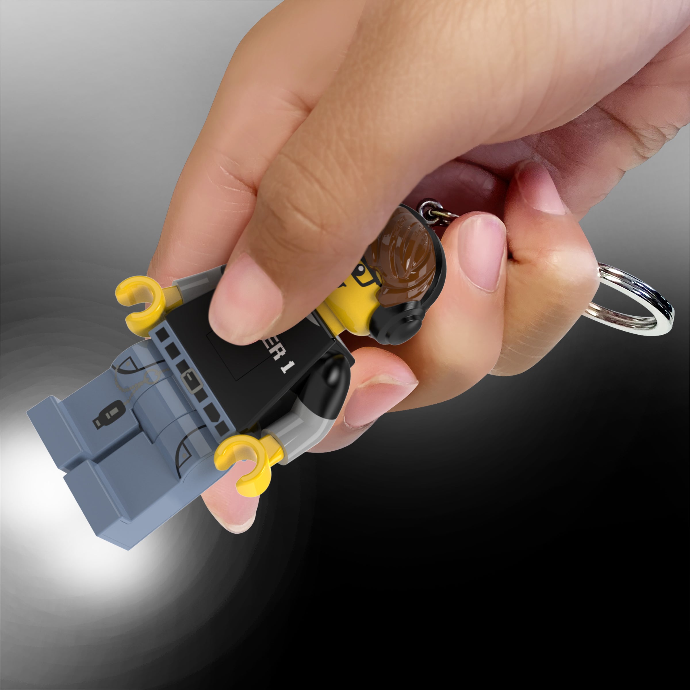 Brelok z latarką LEGO Gamer trzymany w ręce z włączoną latarką świecącą na ciemnym tle