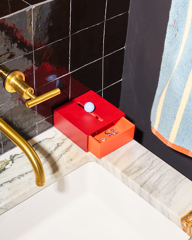 Pojemnik Cache Box Areaware w czerwonym kolorze ustawiony obok umywalki do przechowywania biżuterii