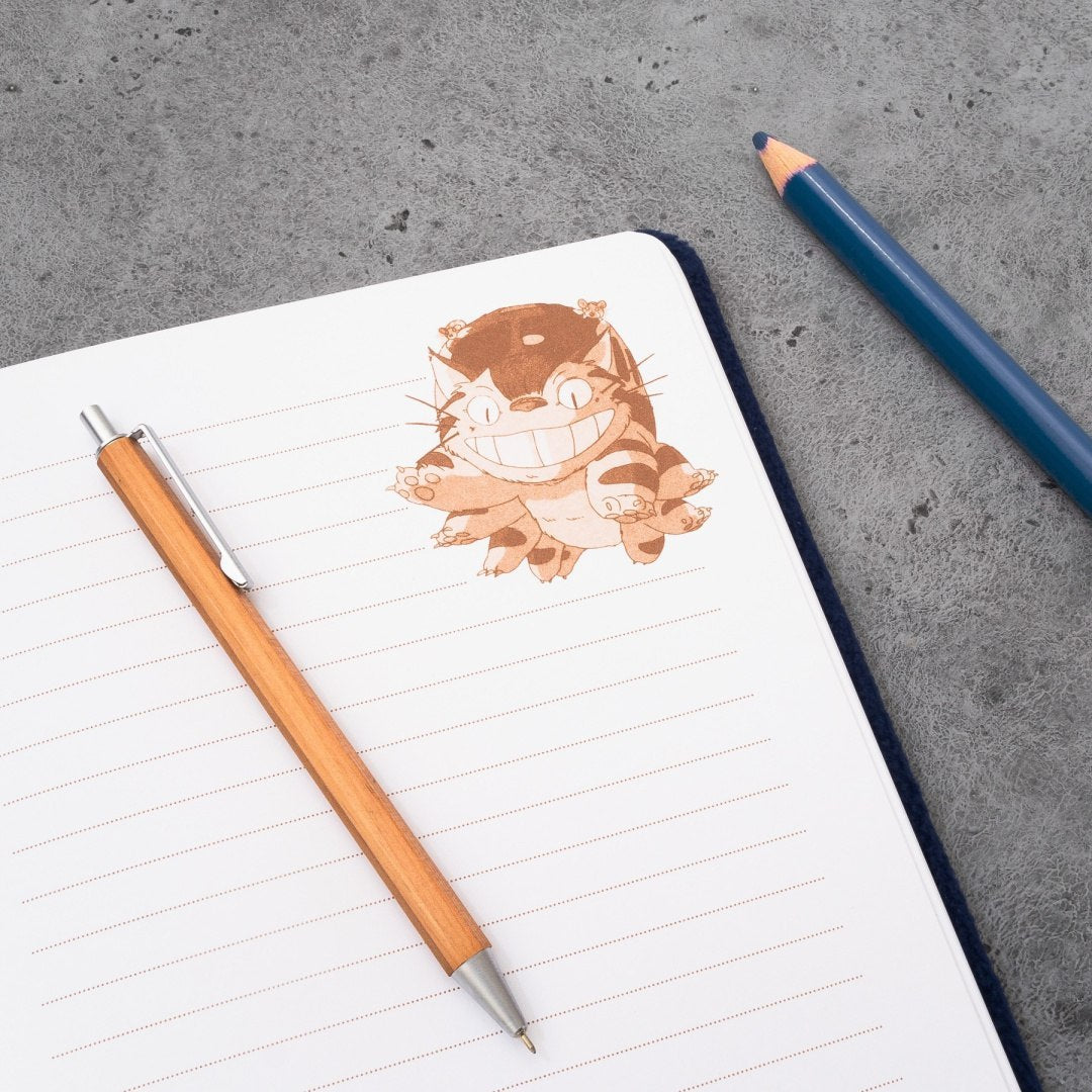 Pluszowy notatnik kotobus z liniowanymi stronami, drewniany długopis i ołówek na szarym tle