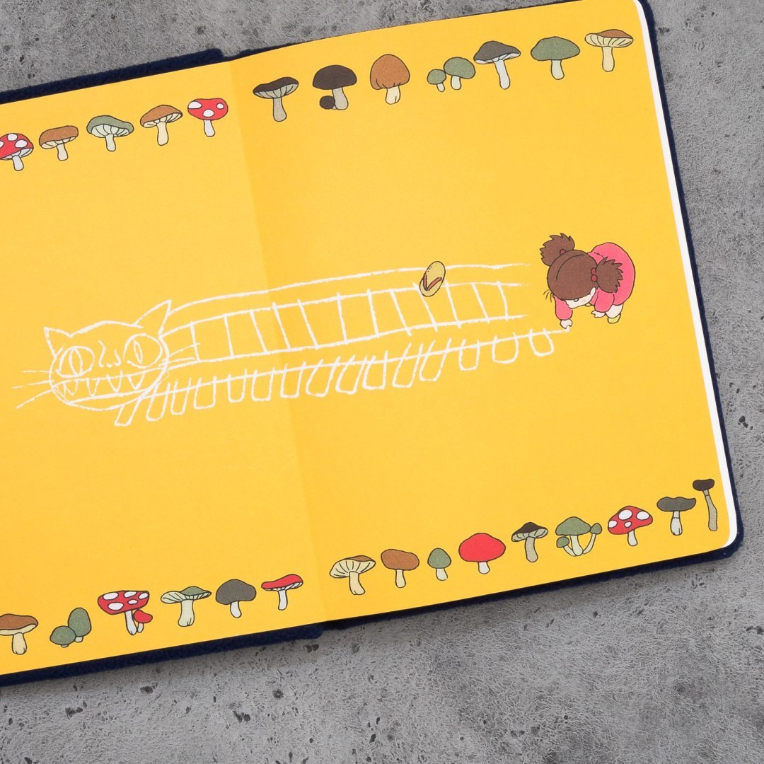 Pluszowy notatnik kotobus z żółtymi kartkami ozdobionymi grzybami i rysunkiem dziecka i kotobusa