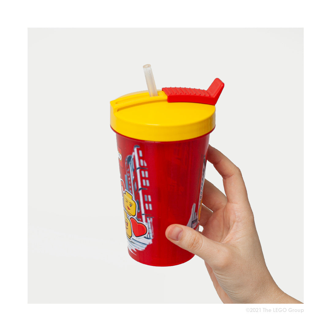 Czerwony kubek LEGO ze słomką dla dziewczynki z żółtą pokrywką trzymany w dłoni