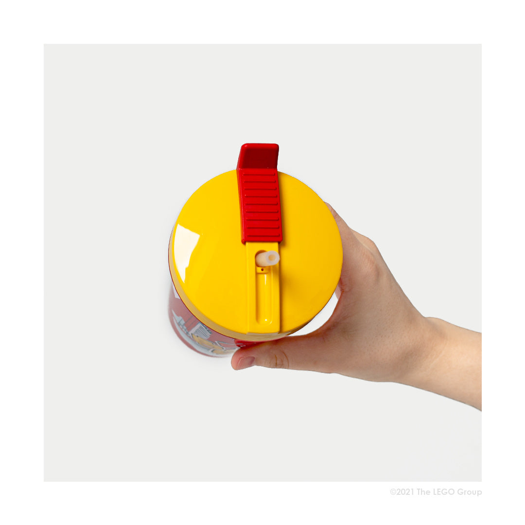 kubek LEGO ze słomką dla dziewczynki z żółtą pokrywką i czerwoną klapką trzymany w dłoni
