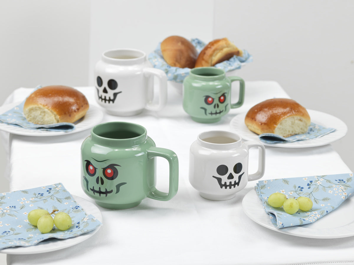 Kubek ceramiczny LEGO Szkieletor w białym i zielonym kolorze na stole z pieczywem i winogronami