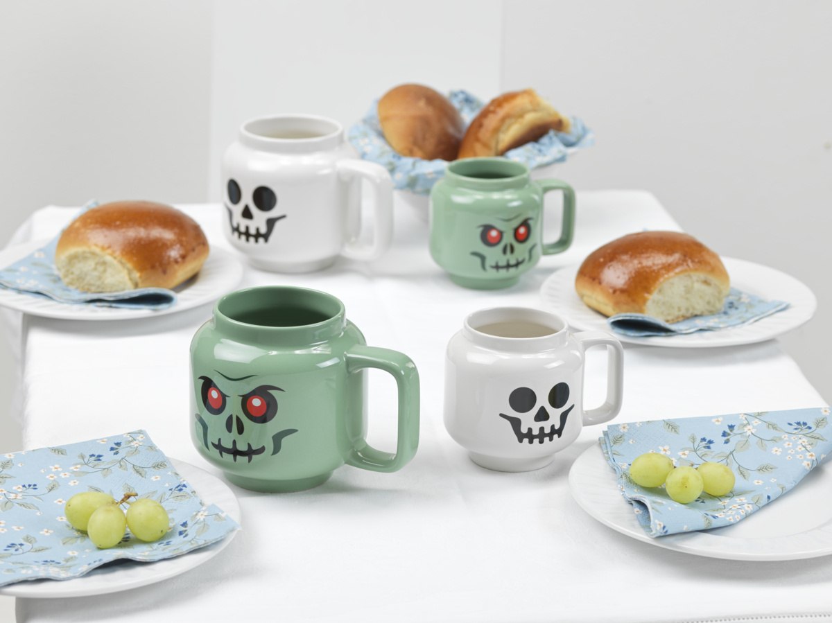 Kubki LEGO zombie w kształcie zielonych i białych czaszek na białym stole z pieczywem i winogronami