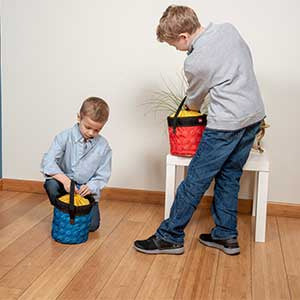 Dzieci bawiące się kubełkami LEGO czerwonym i niebieskim na drewnianej podłodze w domu