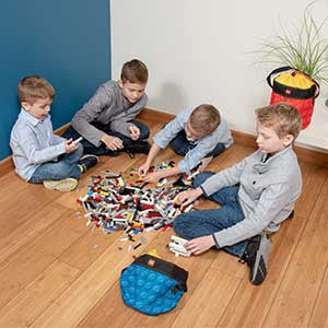 Czterech chłopców bawiących się klockami LEGO z czerwonym kubełkiem LEGO czerwony obok