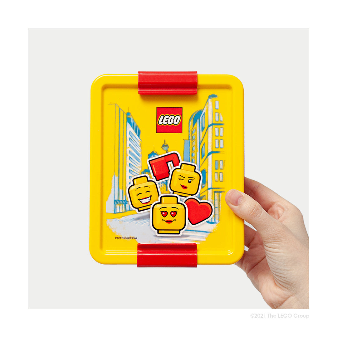 Kolorowy lunchbox LEGO dla dziewczynki z motywem twarzy klocków LEGO i czerwonymi zatrzaskami