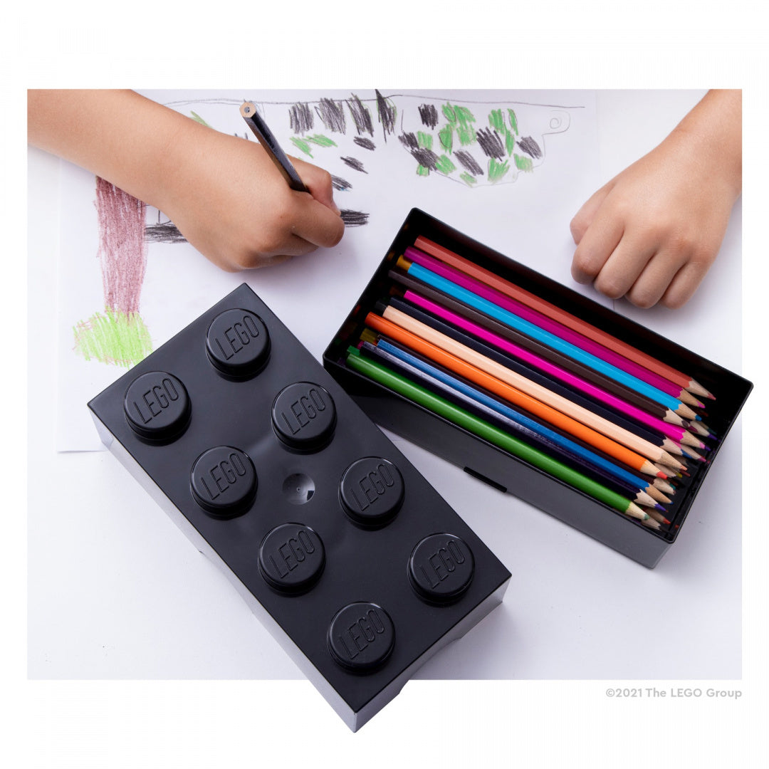 Lunchbox LEGO czarny w kształcie klocka z kolorowymi kredkami i dzieckiem rysującym obrazek