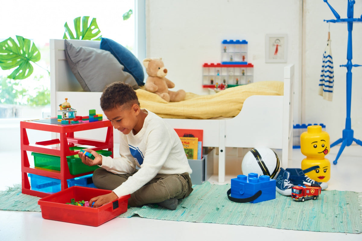 Chłopiec bawiący się klockami LEGO obok czerwonego lunchboxa klocek LEGO w pokoju dziecięcym