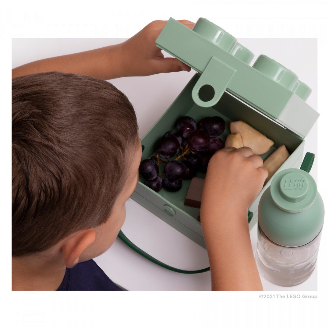 Lunchbox klocek LEGO w kolorze zielonym trzymany przez dziecko z jedzeniem w środku