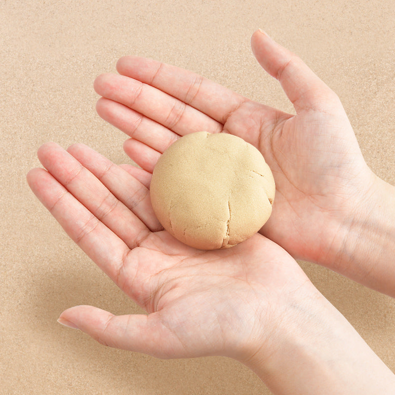 Piasek kinetyczny uzupełnienie 1 kg w formie plastycznej masy trzymanej w dłoniach na beżowym tle