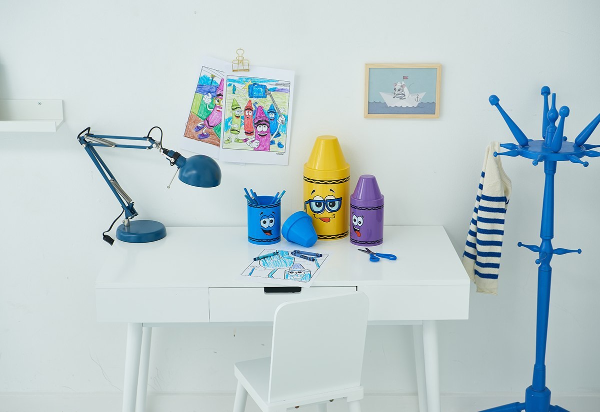 Pojemnik na kredki Crayola fioletowy w kształcie kolorowej kredki na białym biurku