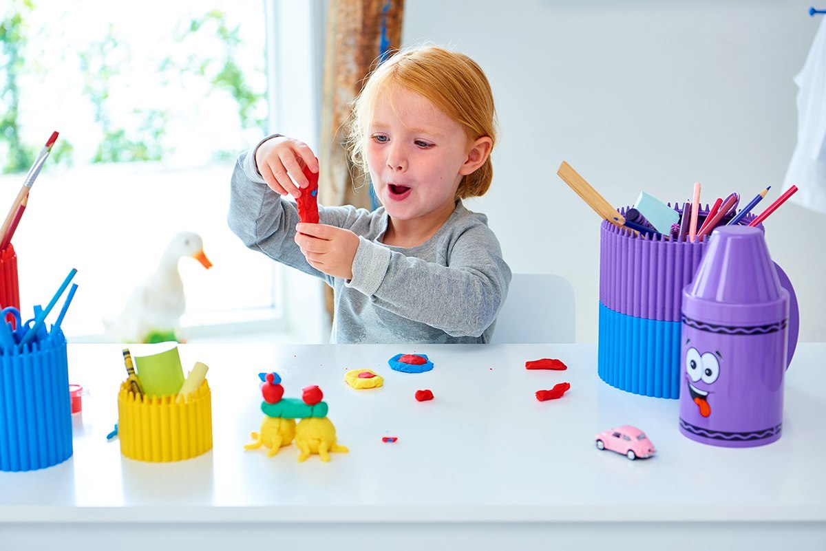 Pojemnik kredka Crayola różowy na biurku z kolorowymi akcesoriami i dzieckiem bawiącym się plasteliną