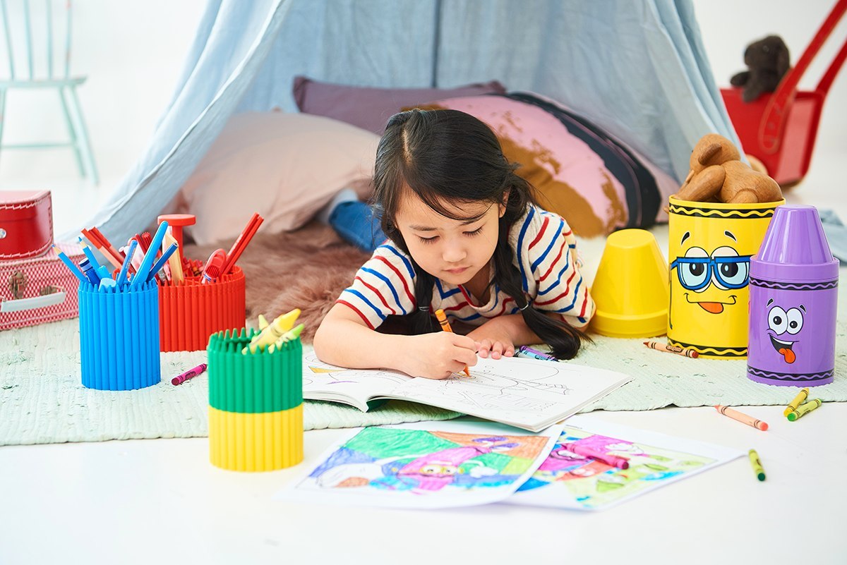 Pojemnik na kredki Crayola zielony z kredkami w pokoju dziecięcym obok dziewczynki kolorującej obrazek