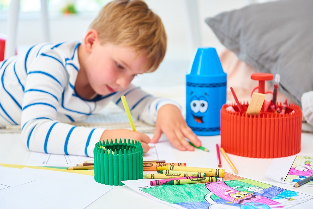 Zielony pojemnik na kredki Crayola zielony marki Yamann na białym stole przy malującym chłopcu