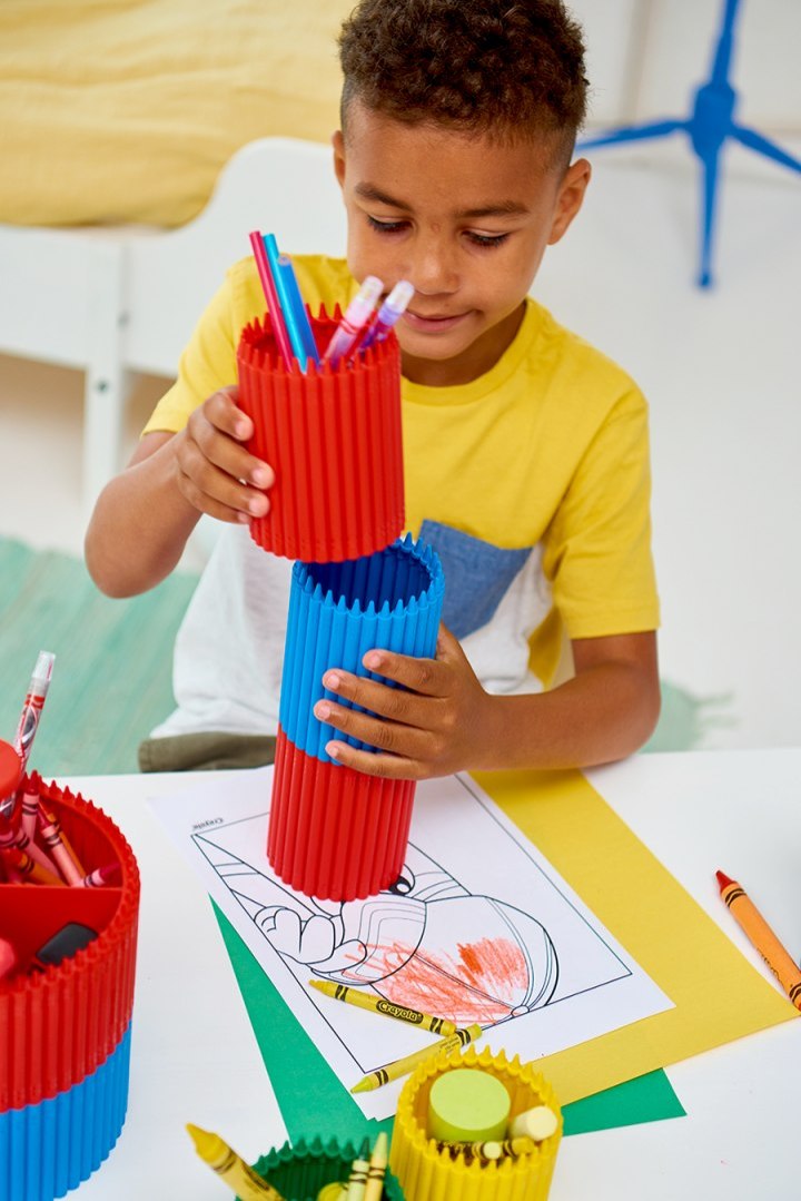 Chłopiec bawiący się małym przybornikiem Crayola czerwonym do przechowywania kredek i markerów