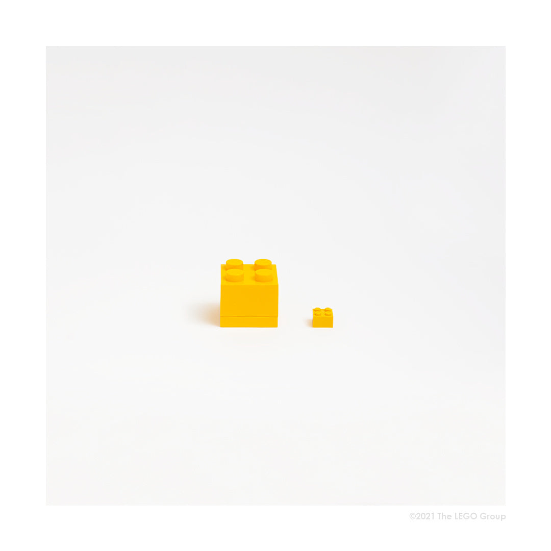 Minipudełko LEGO żółte w kształcie klocka z małym żółtym klockiem obok na białym tle