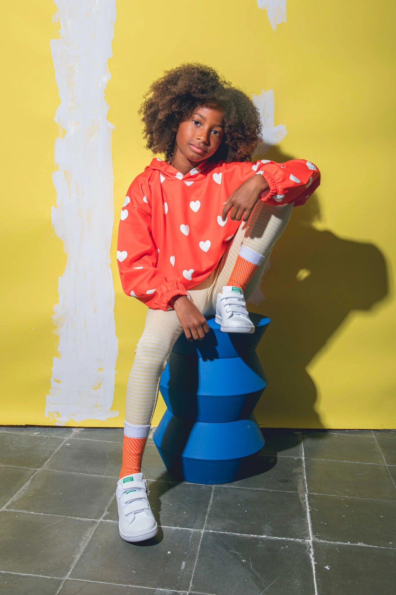 Dziecko w kolorowej bluzie i skarpetki sushi dla dzieci w biało-pomarańczowym wzorze na tle żółtej ściany