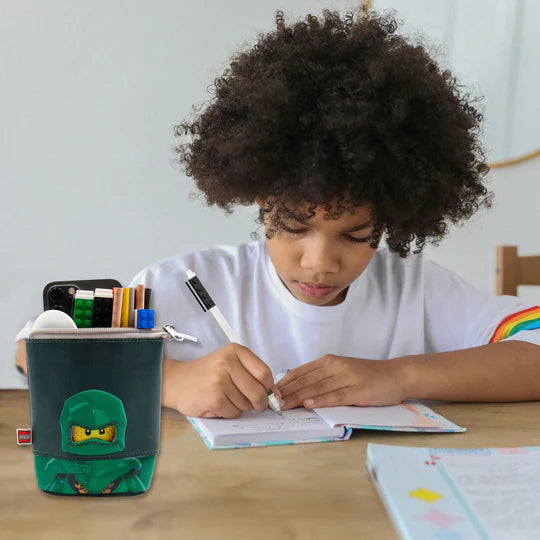Dziecko pisze przy biurku z piórnikiem LEGO Ninjago Lloyd na stole obok zeszytu