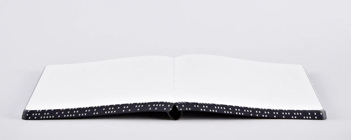 Notatnik graficzny L otwarty na białym tle z czarną okładką w białe kropki