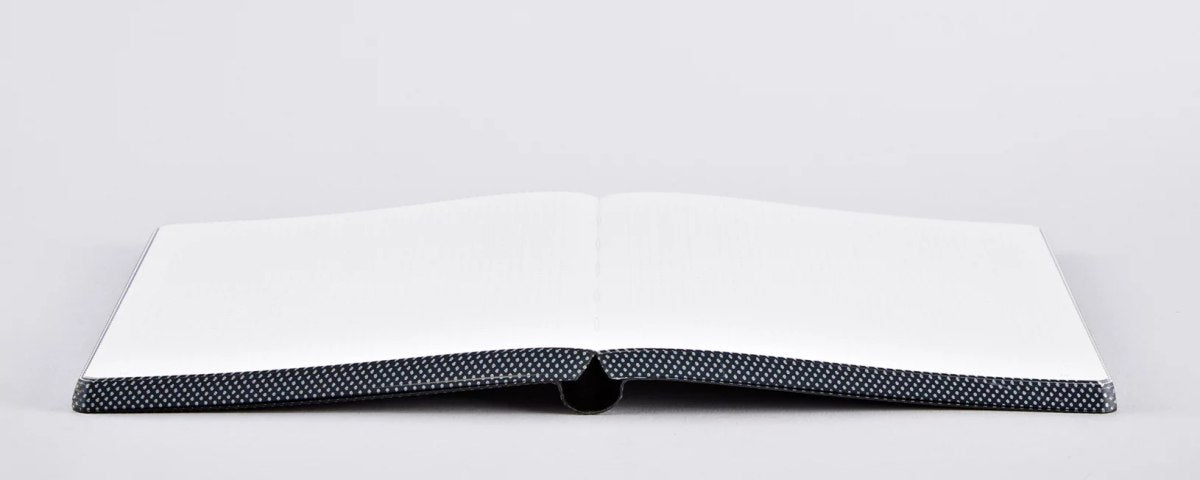 Notatnik Everything Starts From A Dot otwarty na płaskiej powierzchni z czarną kropkowaną okładką