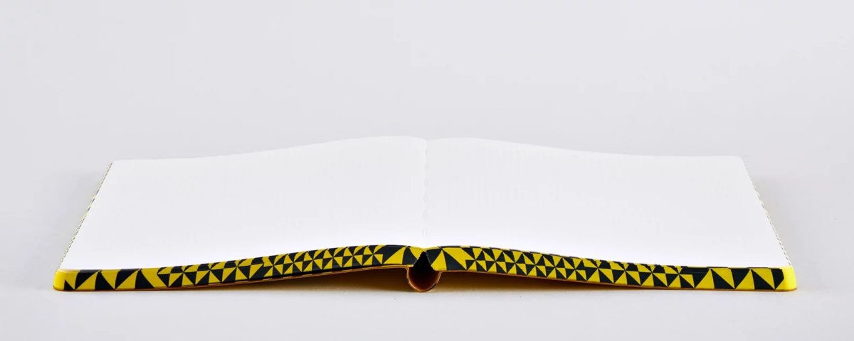 Otwarty notatnik The Happy Book z pustymi białymi stronami i geometryczną żółto-czarną okładką