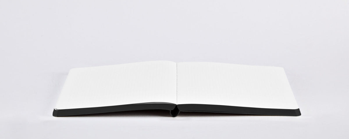 Otwarty notatnik graficzny Jim z czarną okładką i pustymi białymi stronami na białym tle