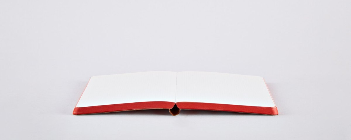 Otwarty notatnik love z czerwonymi brzegami pustych białych stron na jasnym tle