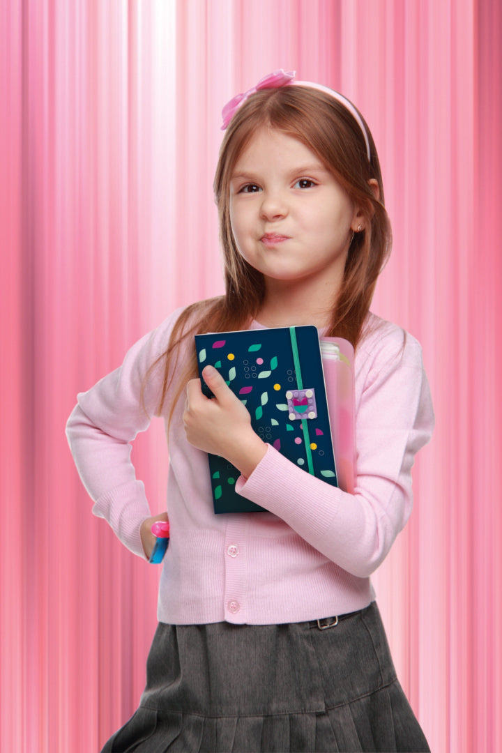 Dziewczynka trzymająca notatnik LEGO DOTS z kolorowymi kropkami na granatowej okładce