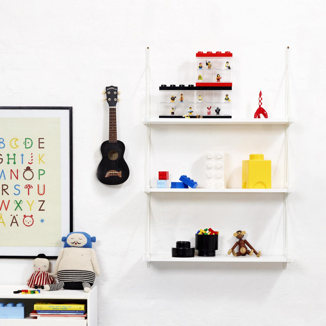 Okrągły pojemnik LEGO czarny na półce w pokoju dziecięcym obok zabawek i książek