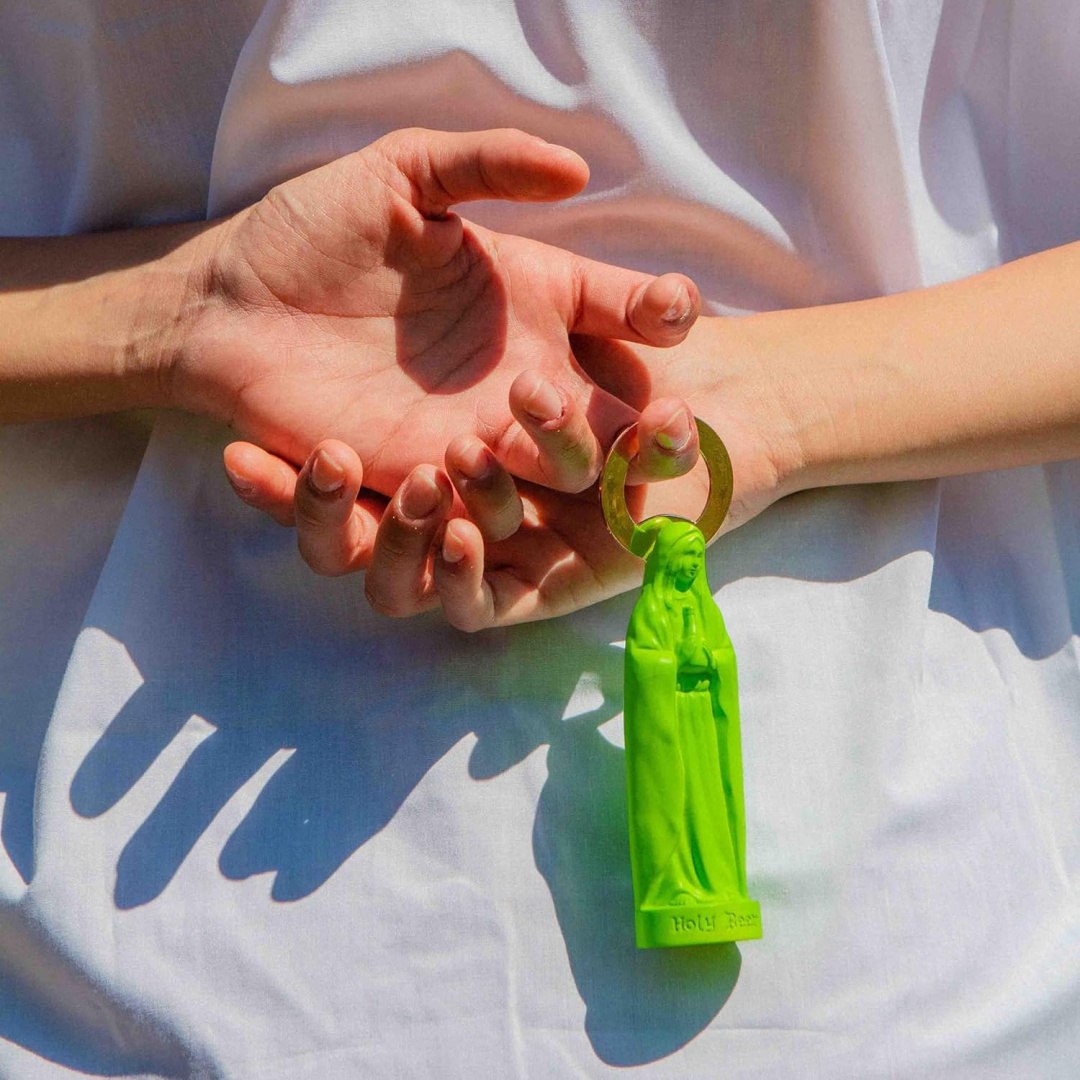 Otwieracz do butelek zielony w kształcie figurki z zawieszką noszony na ręce na jasnym tle