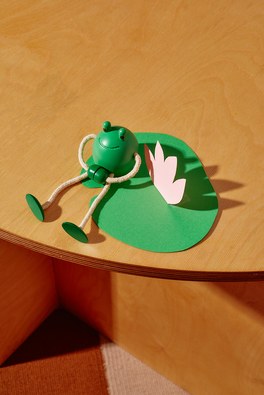 drewniana figurka żaba w zielonym kolorze leżąca na stołu z papierowym liściem