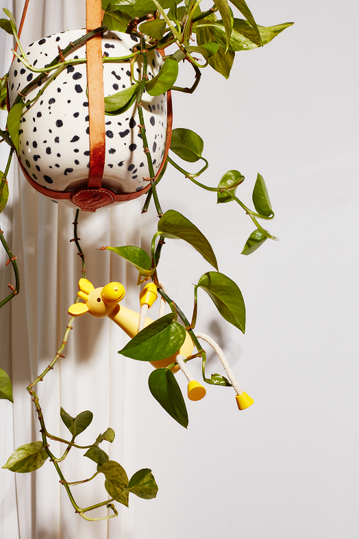 Żółta drewniana figurka żyrafa zawieszona na roślinie doniczkowej w białej doniczce